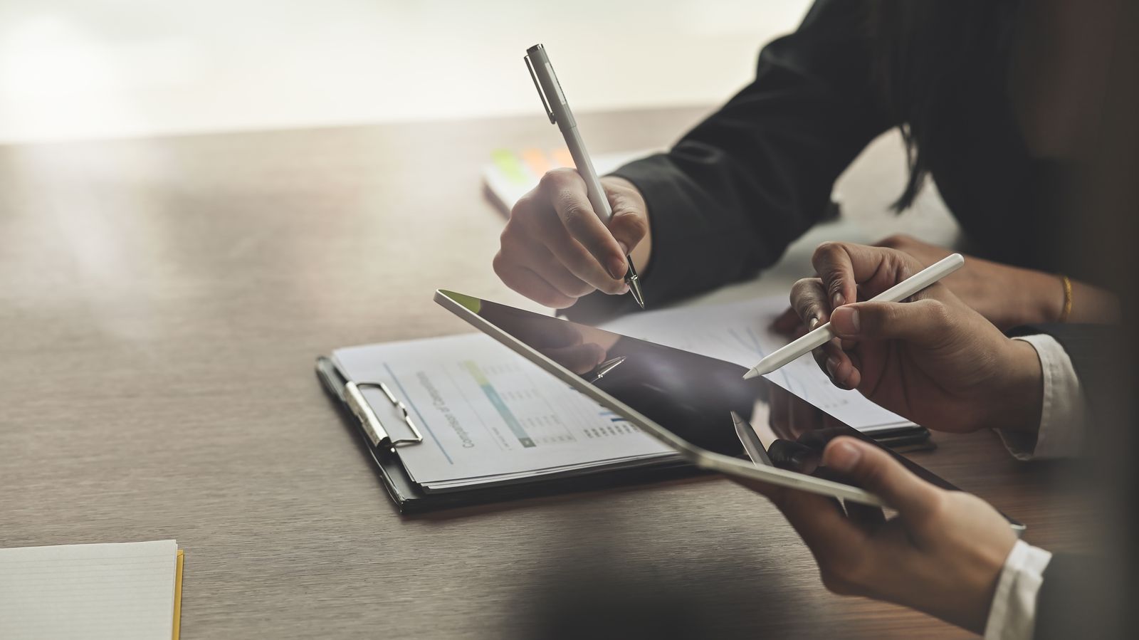 Two people reviewing billing reports across a tablet and paper claim documents